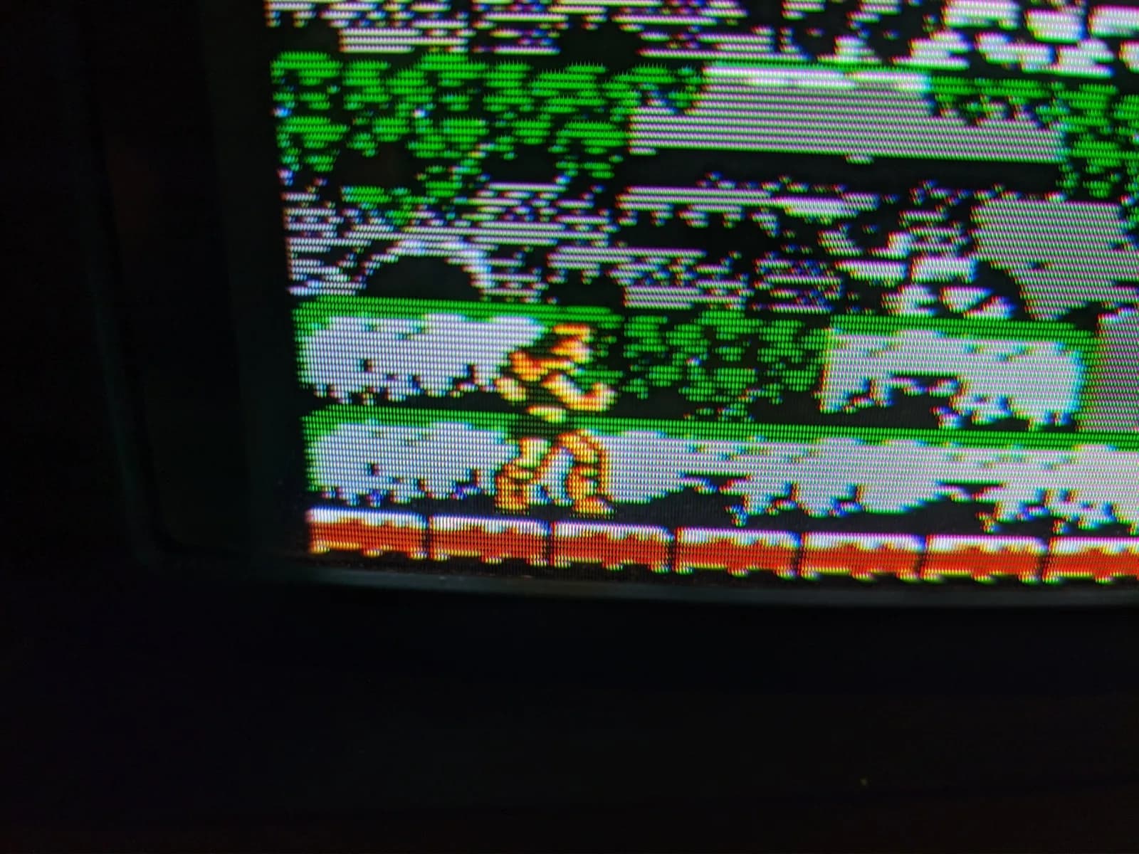 Macro close-up of the Sony BVM-D9H5J's aperture grille, its vertical phosphor stripes visible over a frame of Castlevania III: Dracula's Curse: Trevor Belmont in yellow/tan on a pale floor with green foliage above and a red band below.