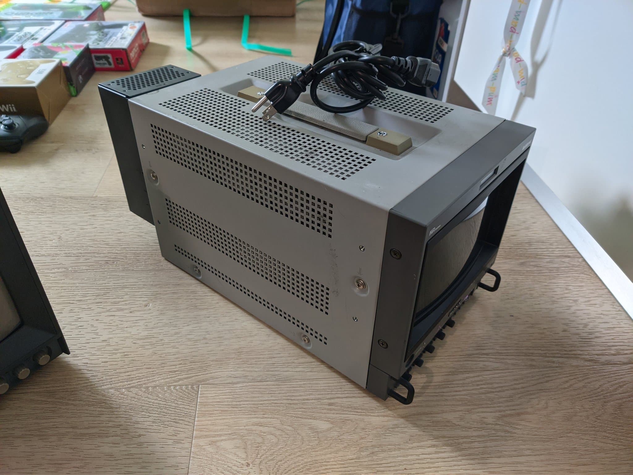 Sony BVM-D9H5J broadcast CRT seen from the side on a wood desk, perforated metal chassis, a small red HR Trinitron badge, coiled power cable on top.