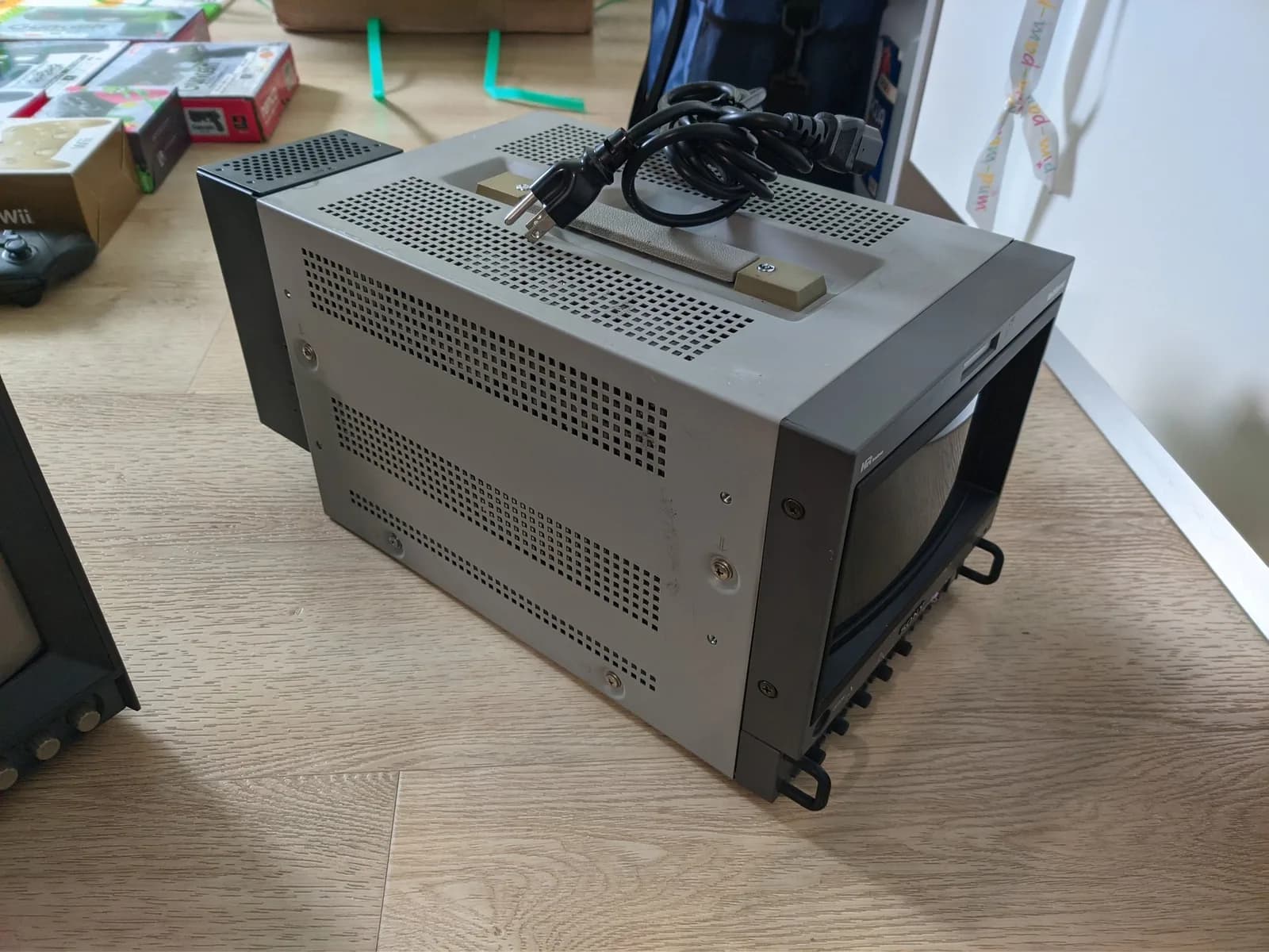 Sony BVM-D9H5J broadcast CRT seen from the side on a wood floor, perforated metal chassis, a small white HR Trinitron badge, coiled power cable on top.