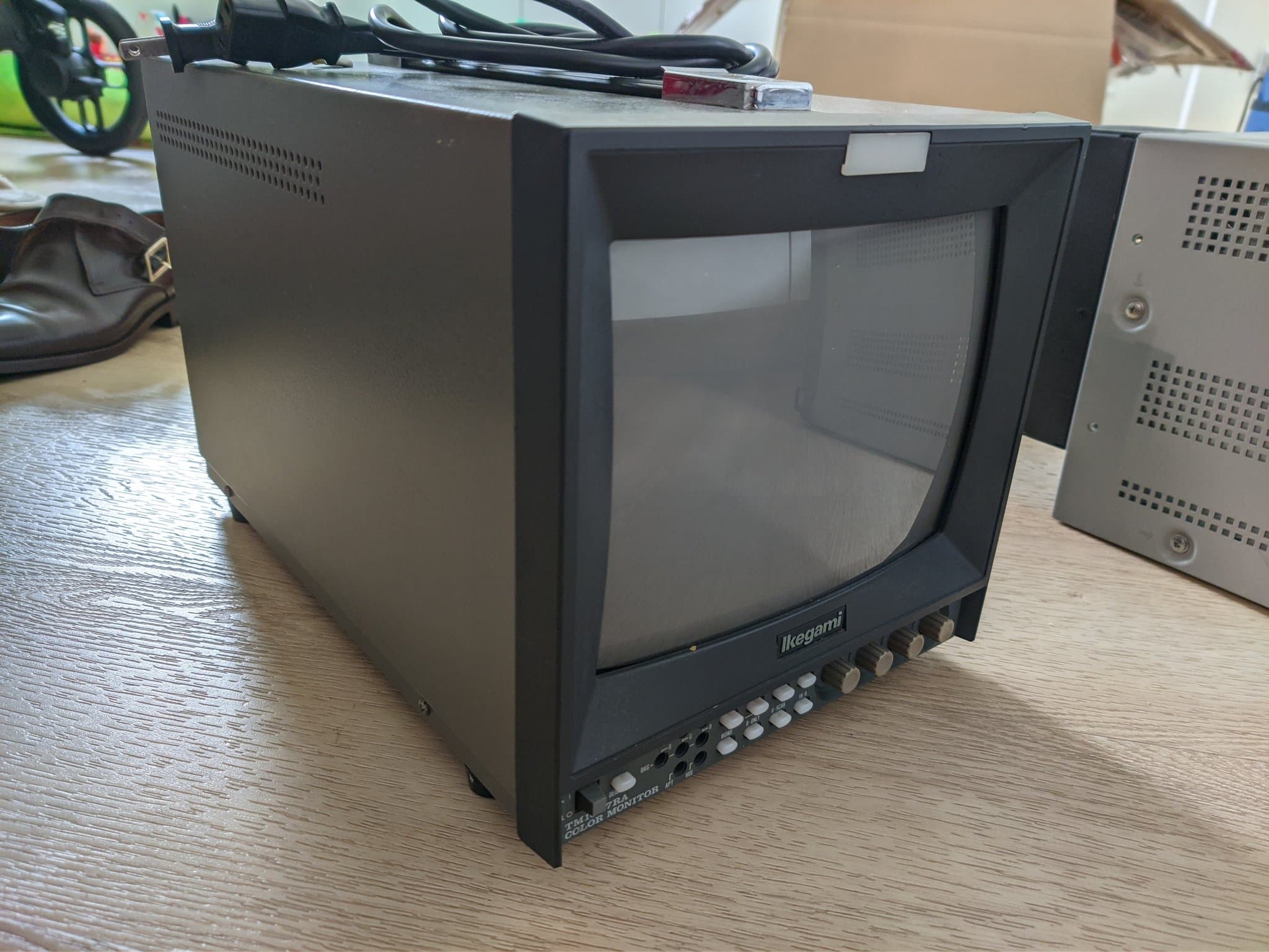 Ikegami TM10-17RA broadcast CRT, front view on a wood desk, blank grey screen, white control buttons and four rotary knobs below the bezel.