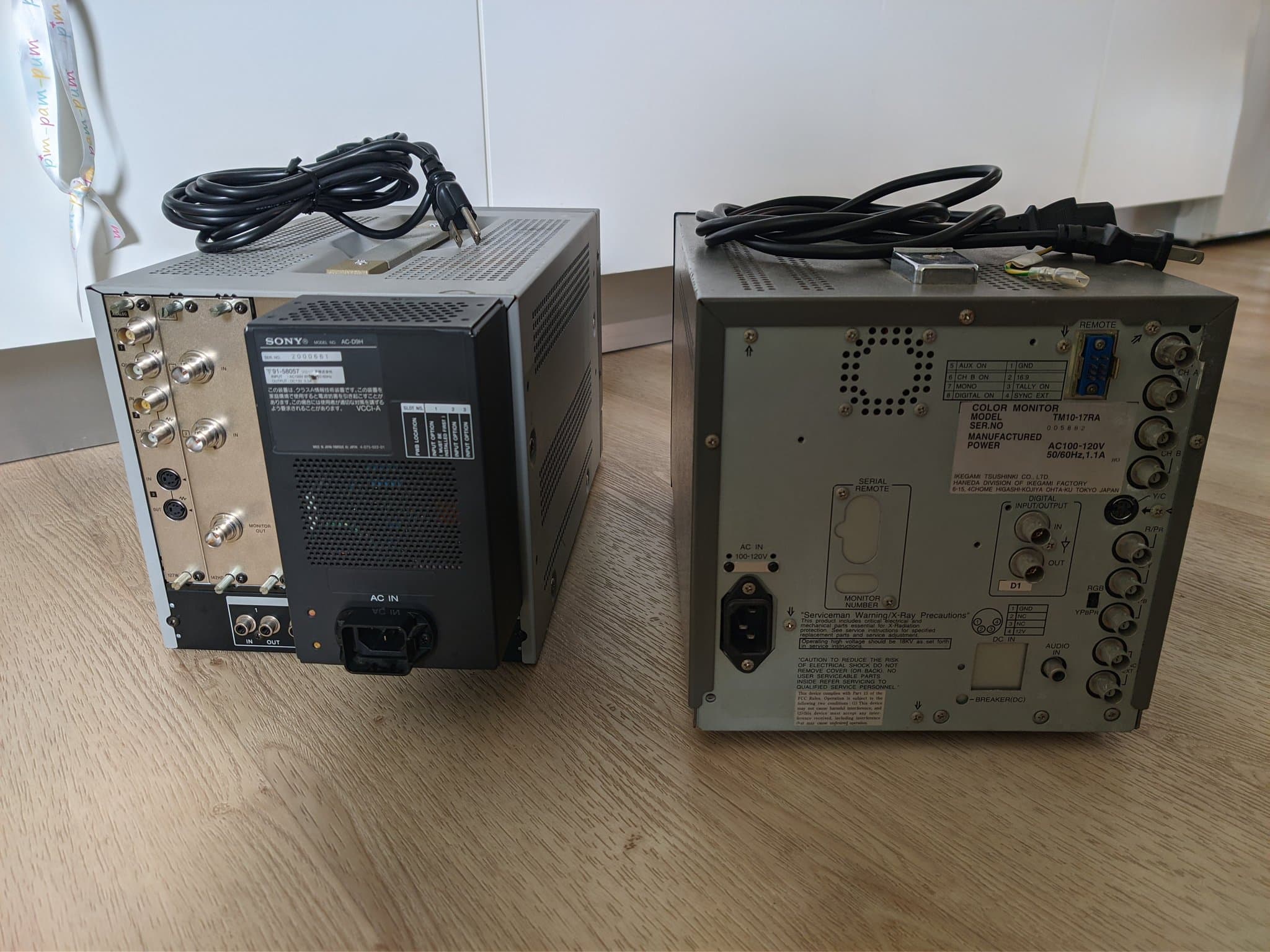 Rear view of two broadcast CRTs on a wood floor: the Sony BVM-D9H5J with its AC-D9H module and input-option slot chart (left), and the Ikegami TM10-17RA with its rear nameplate and BNC inputs (right).