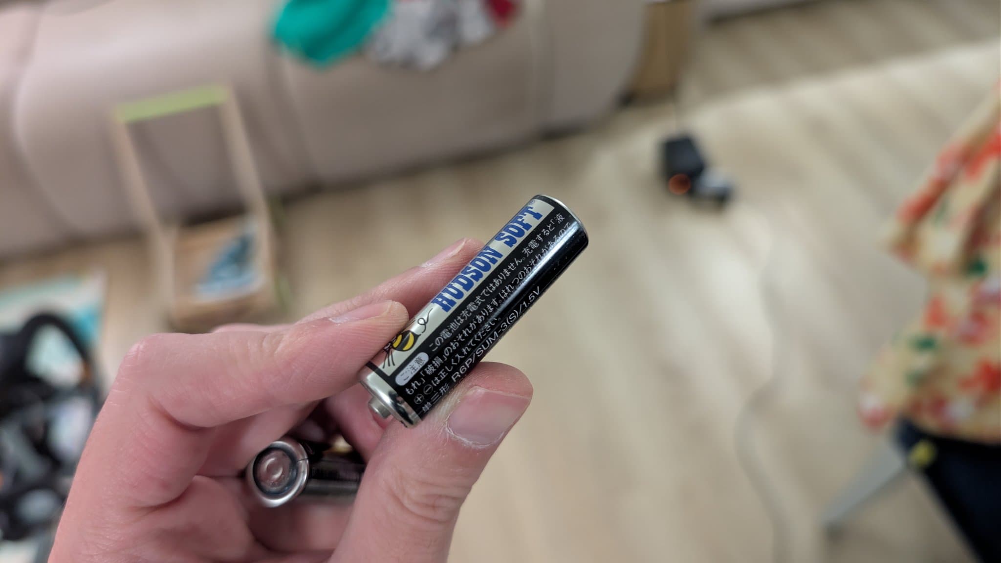 Hand holding original Hudson Soft branded AA battery from Ten No Koe 2, with discharged battery visible below.