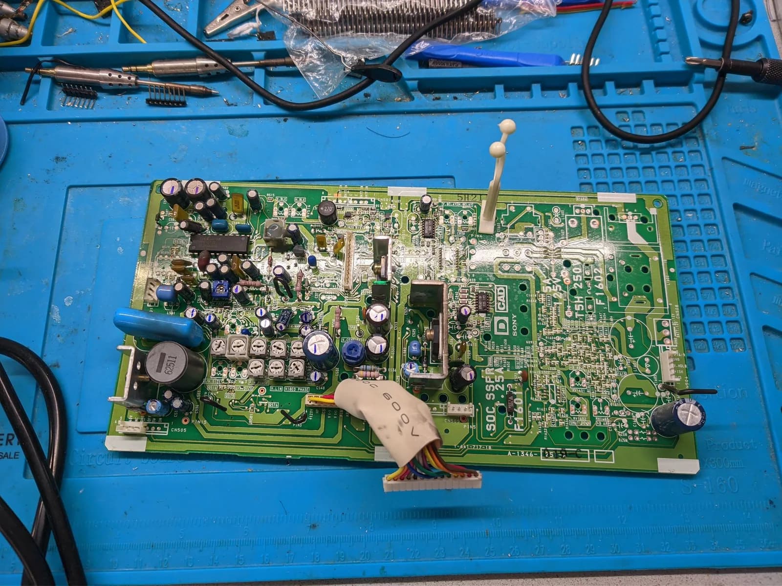 Sony PVM-9040 deflection board with capacitors and components during recap maintenance on blue work mat with tools.