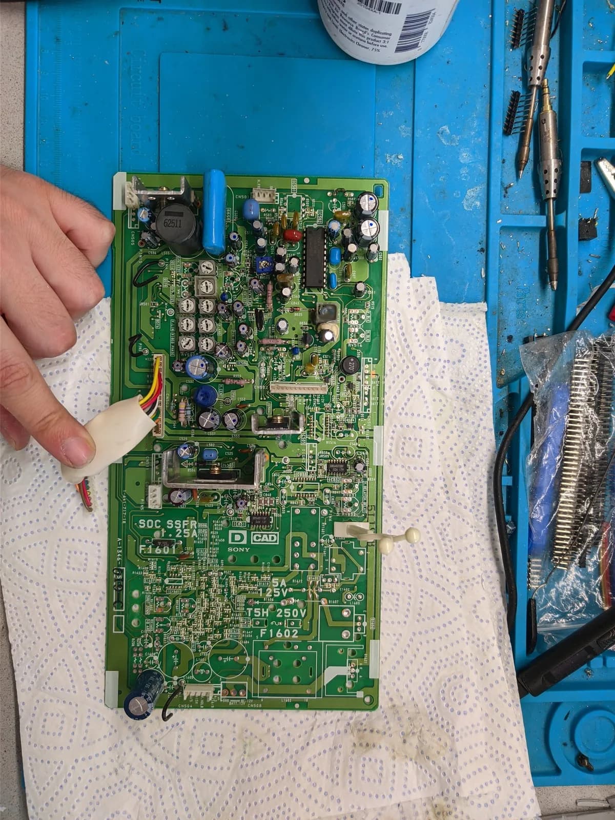 Close-up of Sony PVM-9040 circuit board held in hand, showing green PCB with components, capacitors, and connectors during repair work.