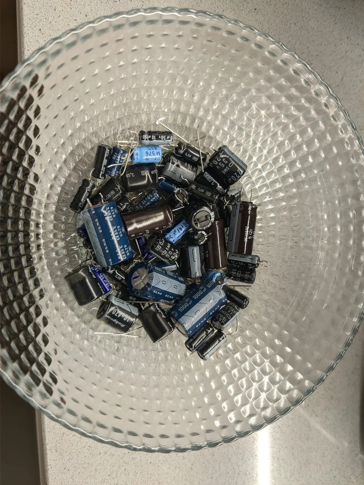 Basket of 51 failed electrolytic capacitors removed from three Sony PVM-9040 monitors during restoration, blue and black cylindrical components.