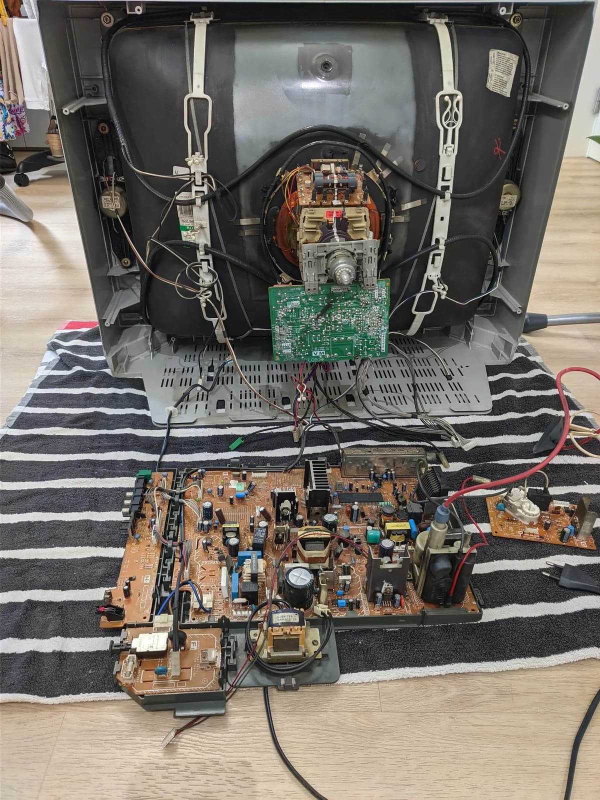 Sony KV-29FX30E CRT TV deshelled but standing upright on a striped beach towel, the bare picture tube with its neck and deflection yoke exposed, and the main chassis board plus the smaller C board removed and laid out on the towel in front of it.
