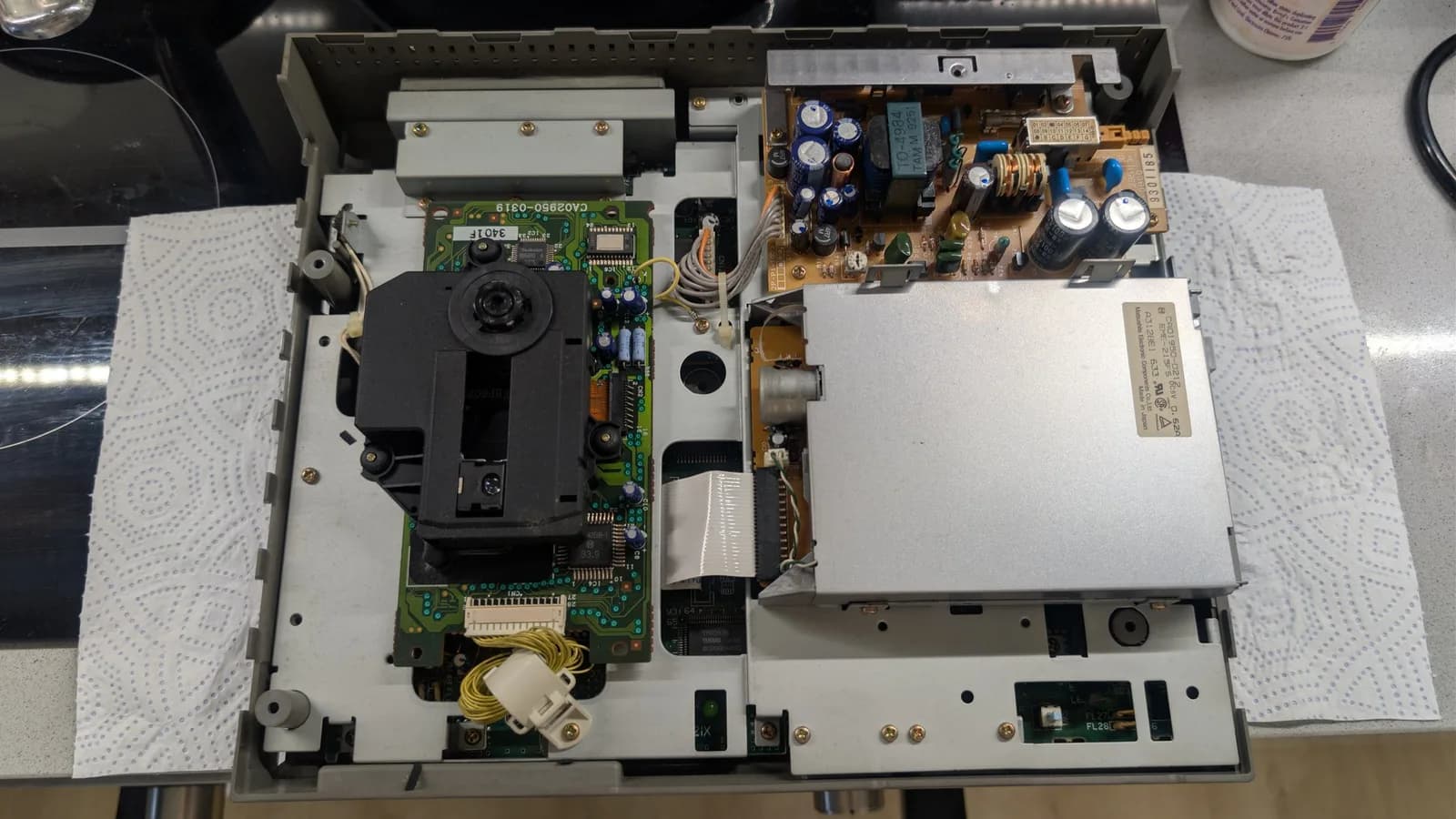 Interior of FM Towns Marty showing recapped power supply and logic boards with green PCBs, capacitors, and floppy drive mechanism during restoration.