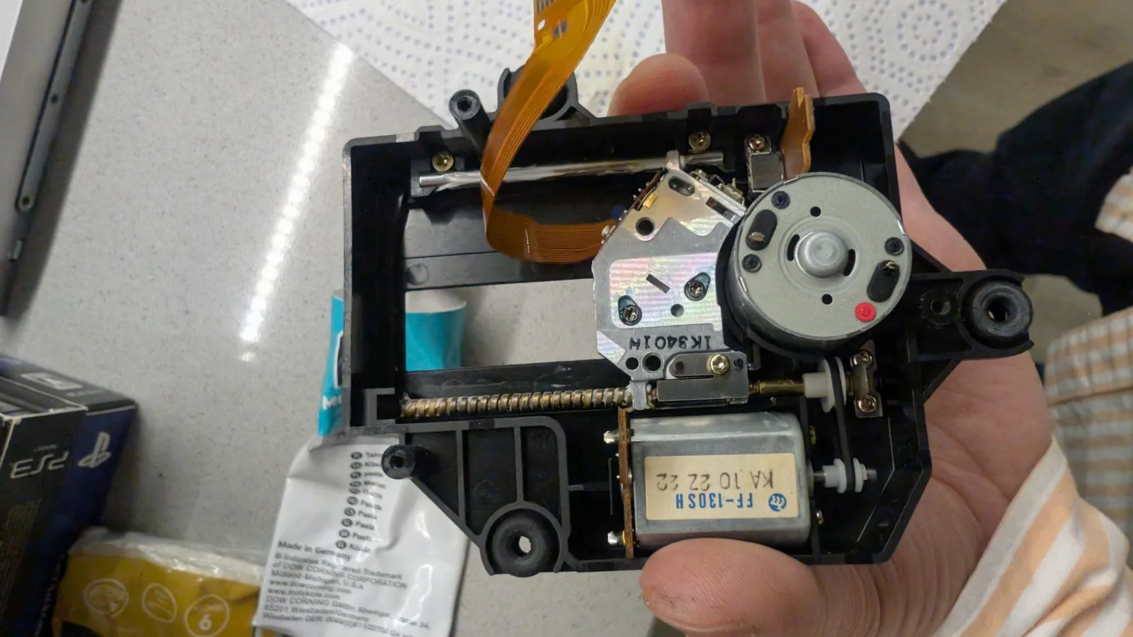 Disassembled FM Towns Marty CD-ROM drive PCB held in hand, showing motor, flex cable, laser lens assembly, and motor control components during recapping.