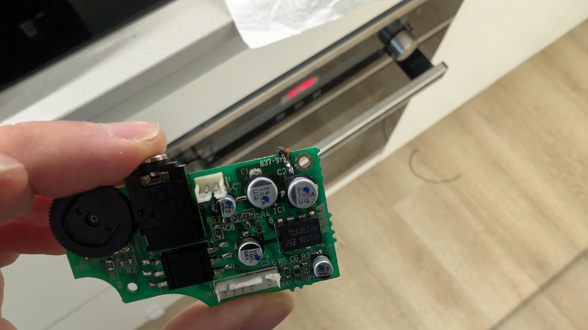 Close-up of Game Gear audio circuit board held in hand, showing broken vias on ground plane and electrolytic capacitors.