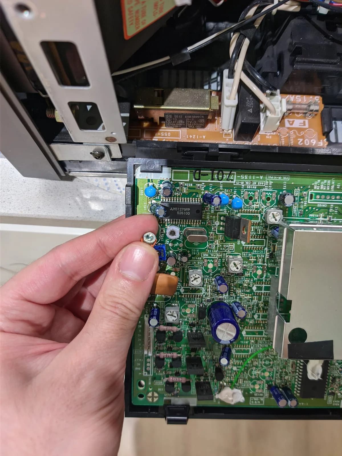 Close-up of hand holding trim potentiometer over green circuit board during PVM-9040 color restoration repair.
