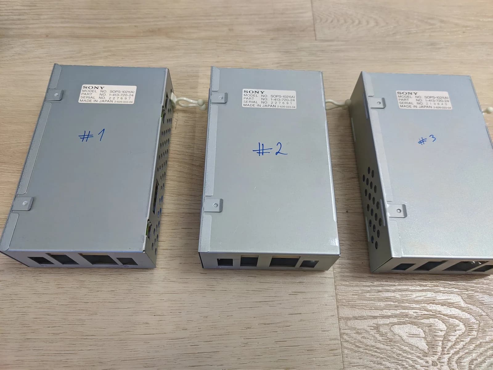Three Sony PVM-9040 power supply units labeled #1, #2, #3 lined up on wooden floor, showing exterior casings and ventilation ports.