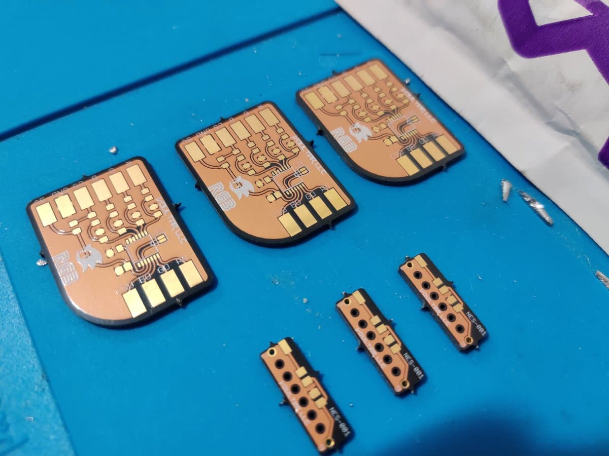 Three assembled Voultar MD RGB bypass boards and four NES expansion audio enabler modules on blue surface, showing gold traces and solder joints.