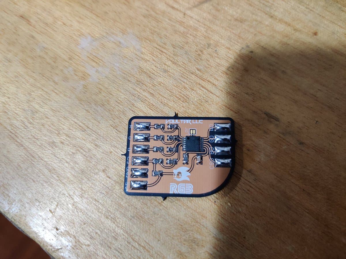 Assembled Voultar MD RGB bypass PCB with six capacitors and central IC chip on wooden surface, first soldering project.