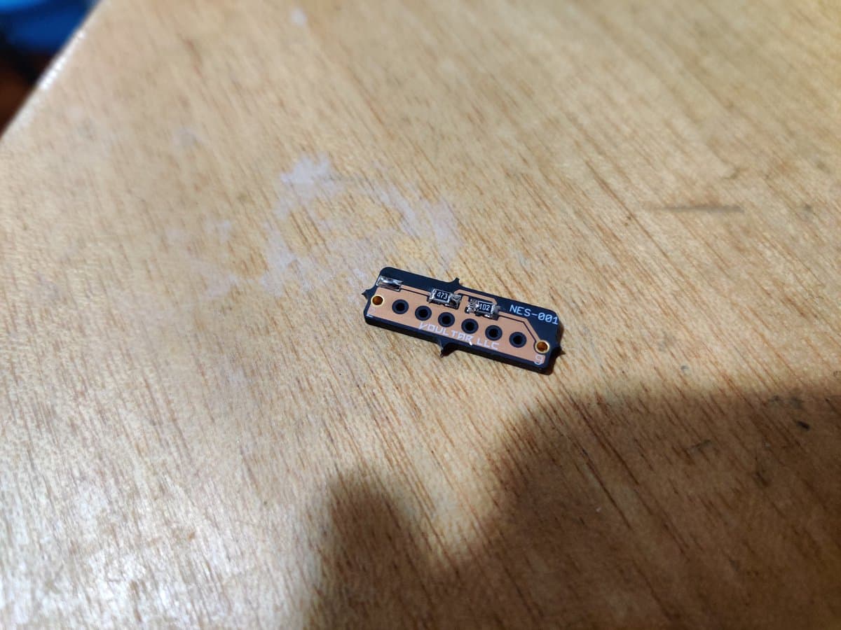 NES-001 expansion audio board with six circular component holes and black PCB mounted on wooden surface, first assembled mod.