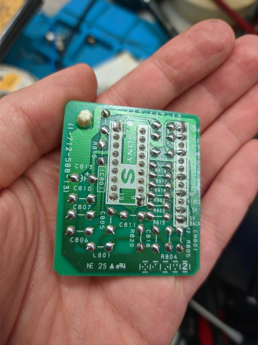 Sony PVM S-board held in hand showing recapped and reflowed capacitors C806-C815, R801-R803, with folded capacitor modification visible.