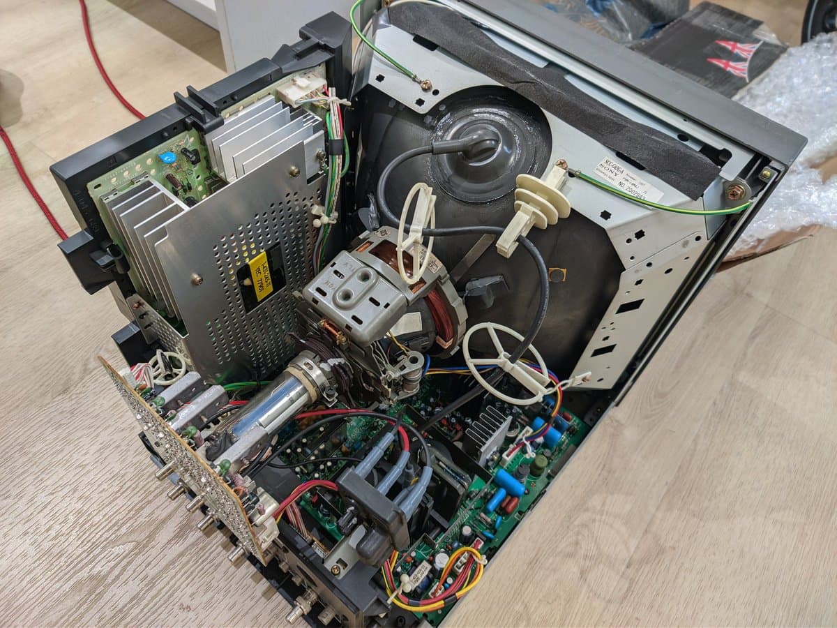 Sony PVM-14M4J internals during reassembly: CRT tube, deflection yoke, power supply, capacitors, and circuit boards with dielectric grease application.
