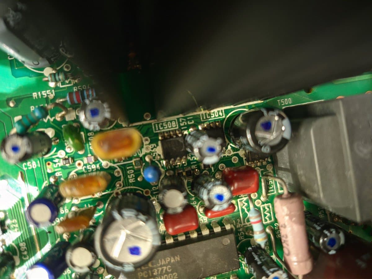 Close-up of Sony PVM-14M4J circuit board showing capacitors, resistors, and IC chips during reassembly and dielectric grease application to anode cap.