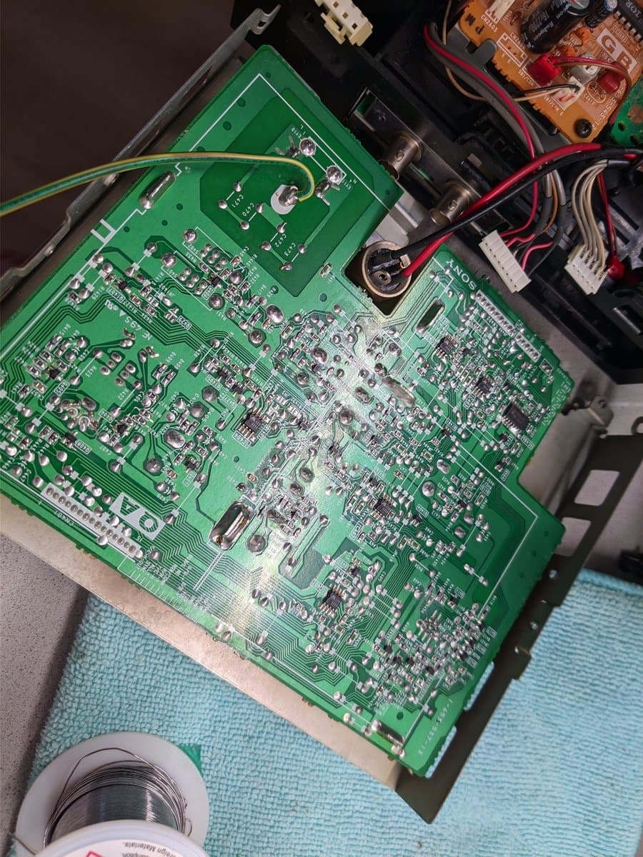 Green PCB with dense component layout, solder joints visible, red and black wires connected to upper section during BVM-9045QD restoration work.