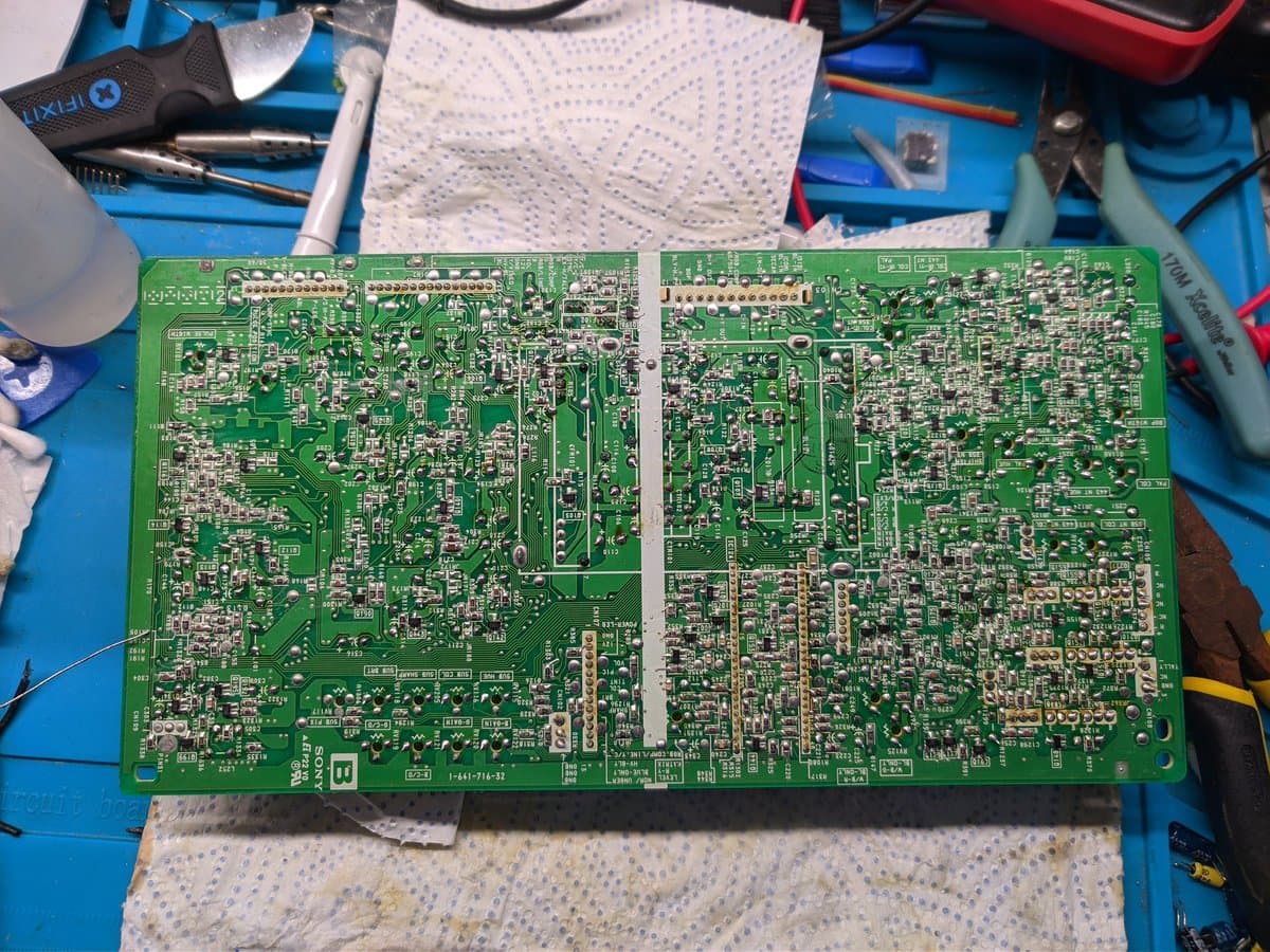 Sony BVM-9045QD colour board underside during reflow repair, showing dense component layout and solder joints on blue work mat.