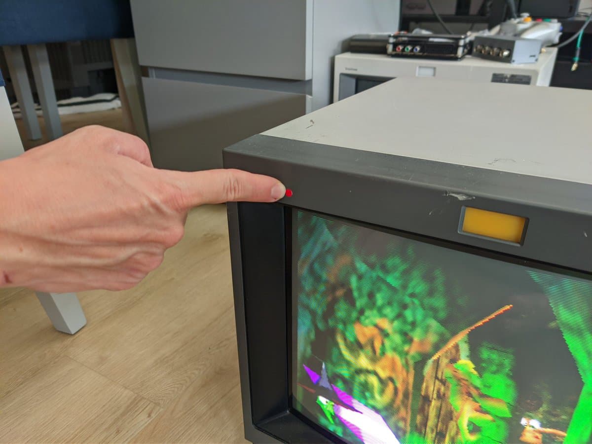Hand pointing to deflection yoke on Sony PVM-14M4J CRT displaying vibrant test pattern; monitor fully repaired and operational.