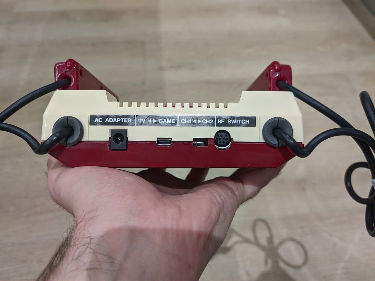 Famicom rear panel showing composite adapter with AC adapter, TV/Game, channel switches, and RF switch ports visible in hand.