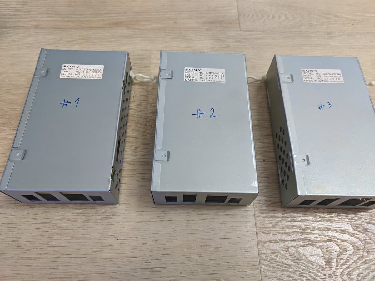 Three Sony PVM-9040 power supply units labeled #1, #2, #3 lined up on wooden floor, showing exterior casings and ventilation ports.