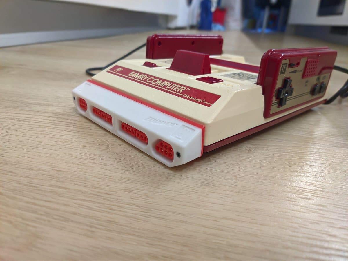 Famicoun NES controller adapter in red and white, displaying controller ports and cable on wooden surface.