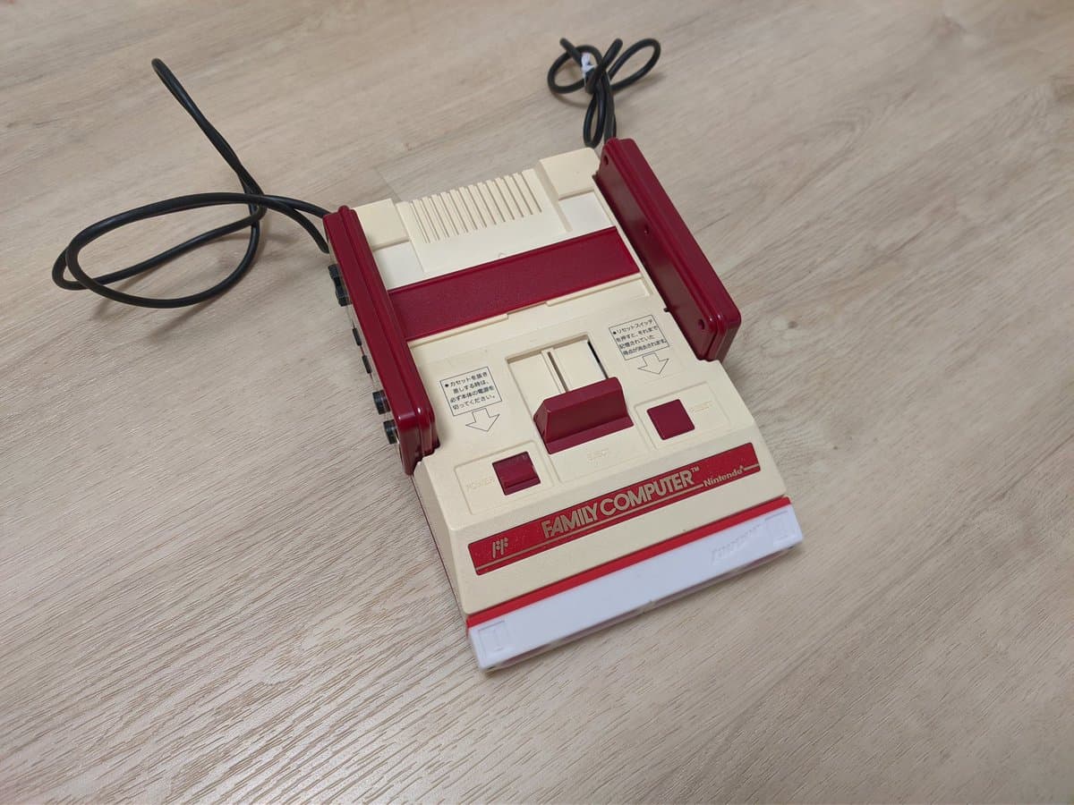 Famicoun controller adapter in red and white, connected to coiled cable with controllers attached, displayed on wooden surface.