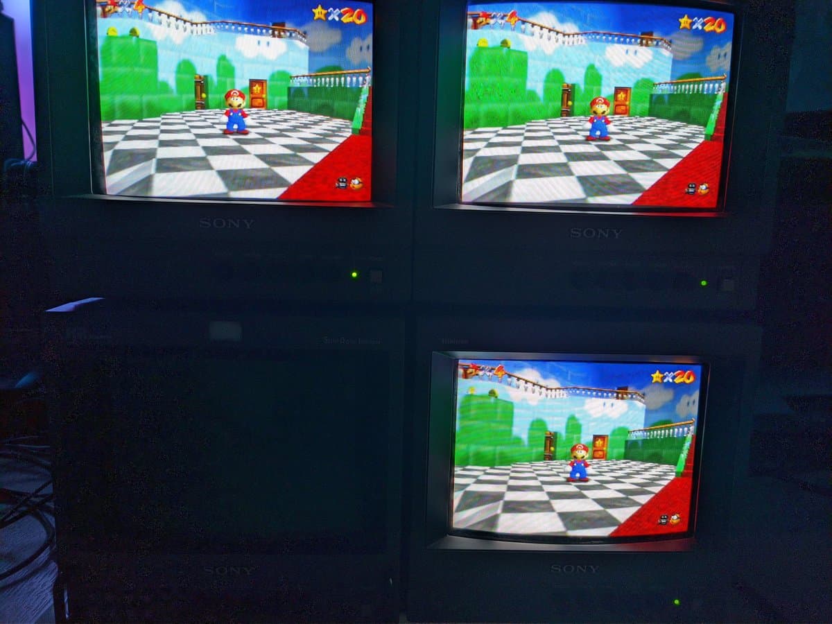 Three Sony PVM-9040 CRT monitors displaying Super Mario 64 via S-video, showing identical castle courtyard scenes with Mario character on checkered floor.