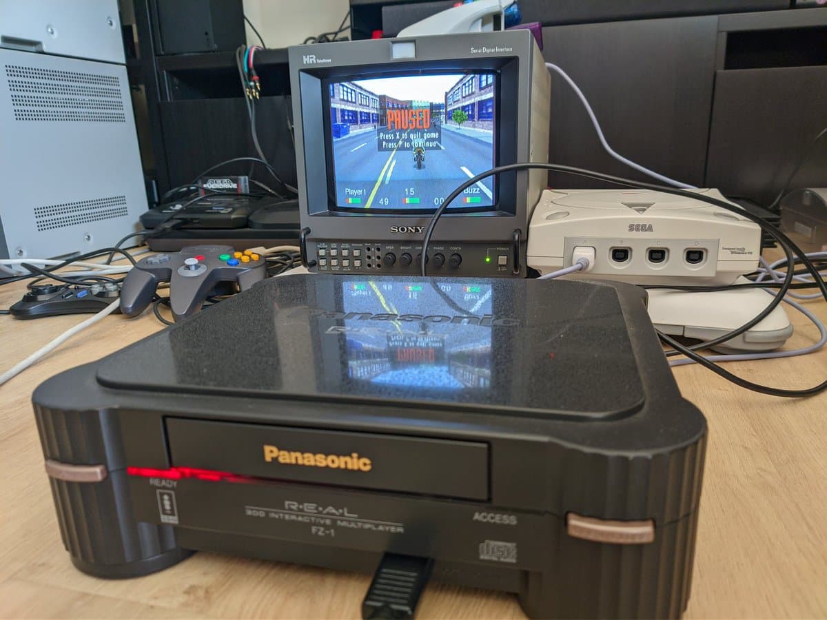 Panasonic FZ-1 3DO console with restored PSU displayed alongside Sony monitor showing Road Rash gameplay, Sega Dreamcast, and arcade controller on wooden desk.