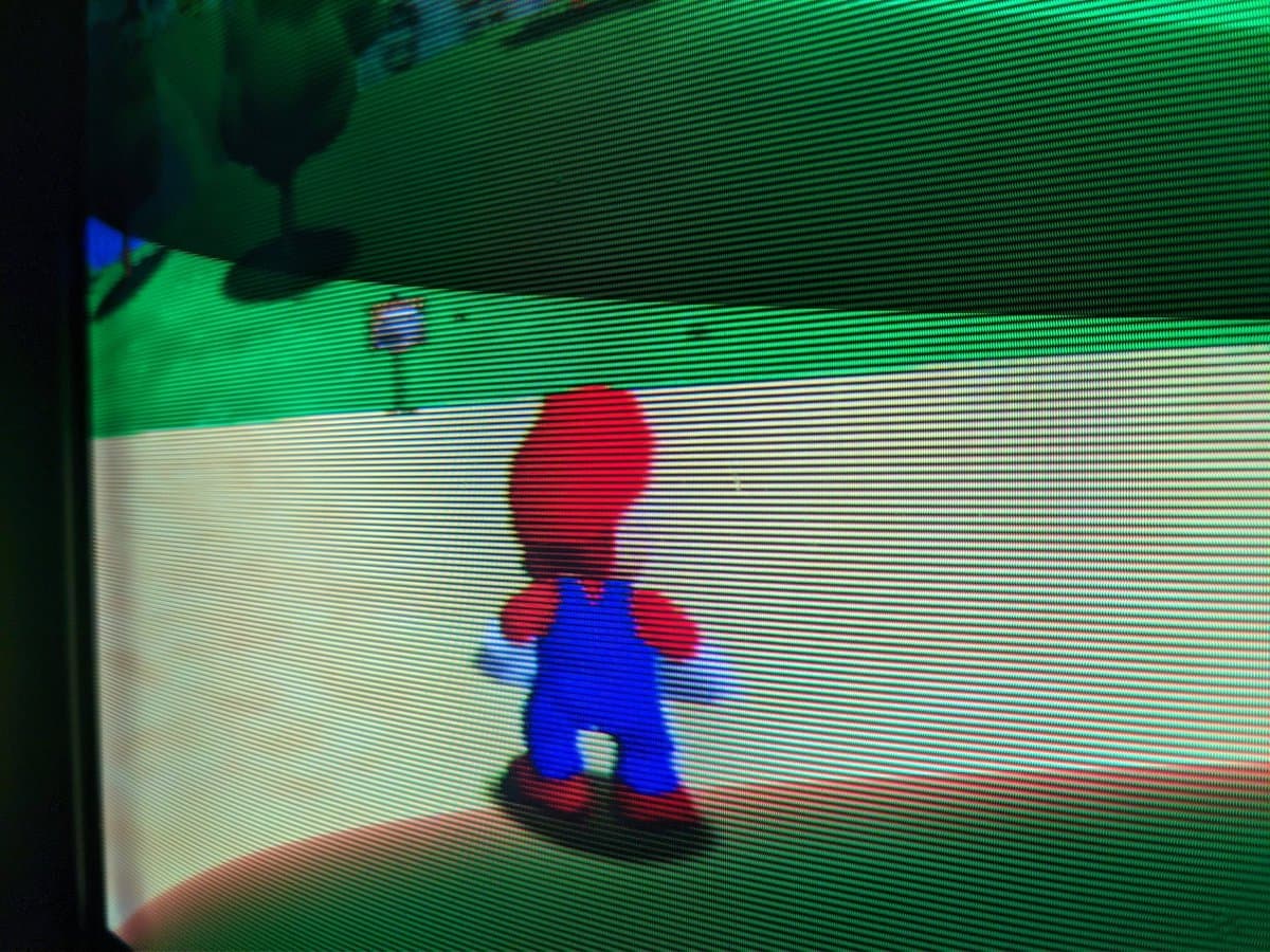 Pixelated CRT display showing Super Mario character in blue overalls and red shirt on green background via composite video input on Sony BVM-D14H1E monitor.