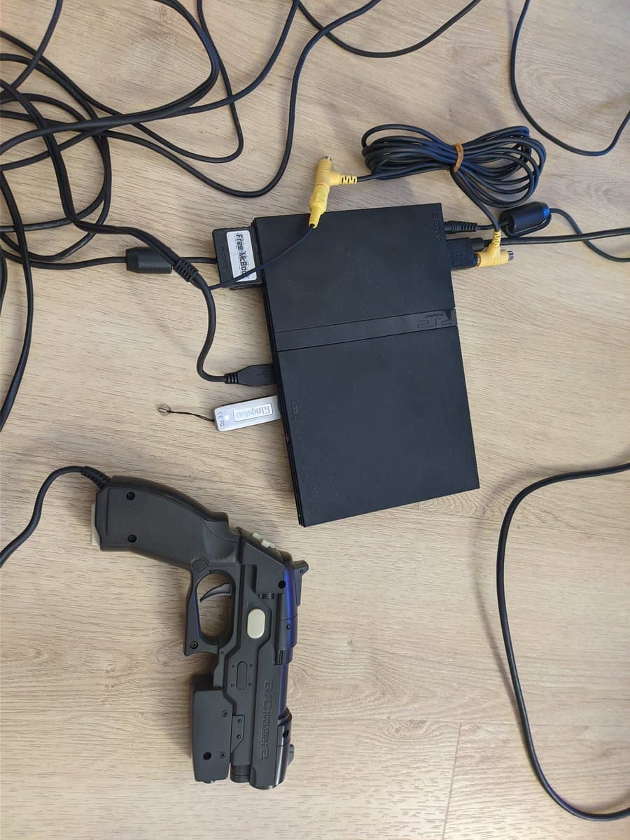 GunCon 2 light gun with connected cables and black composite/AV connectors displayed on wooden surface during maintenance.