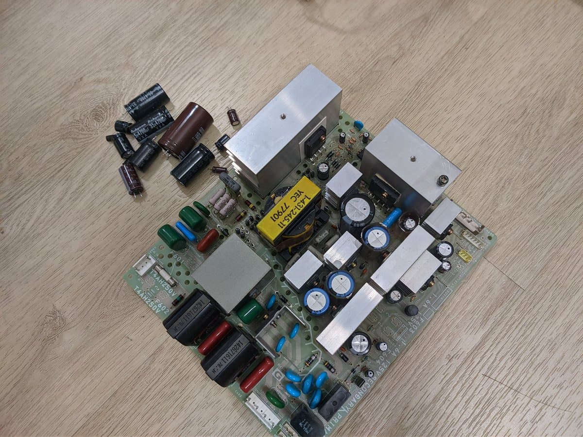 Disassembled Sony PVM power supply boards with electrolytic capacitors removed, showing recap work in progress on green PCBs with white heatsinks.