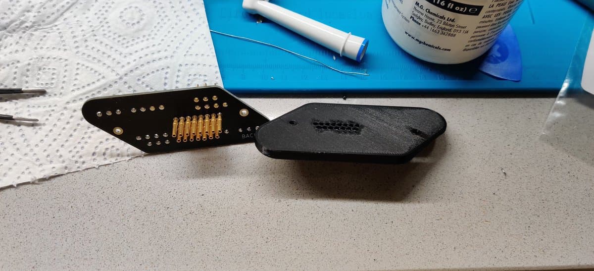 Twin Famicom wireless controller connector with gold-plated pins and black plastic housing, alongside repair supplies on workbench.