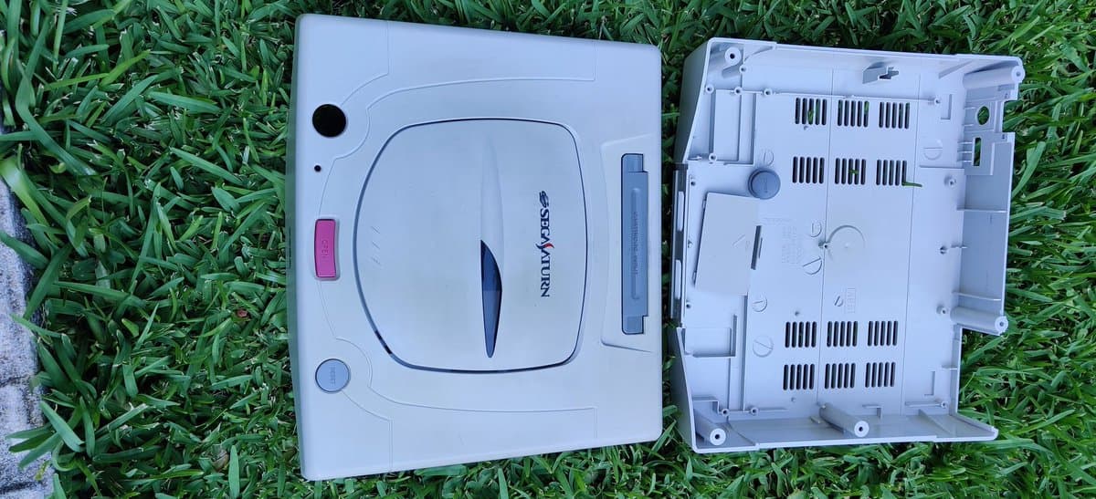 Sega Saturn Model 2 casing before and after hydrogen peroxide retrobrighting treatment, showing yellowed plastic restoration progress.
