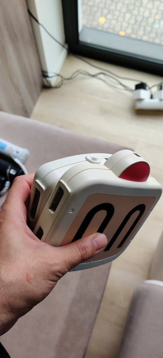 Hand holding white Sega Master System controller with red thumb pad, showing retrobrighting results on desk.