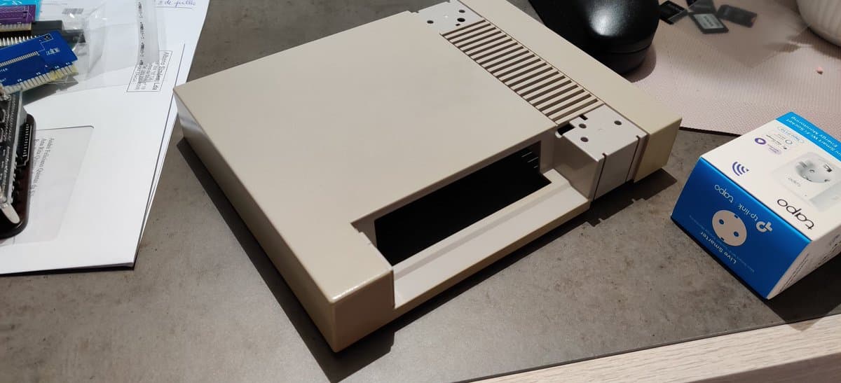 Vintage Apple computer with open disk drive bay, alongside retrobrighting supplies and blue storage packaging on workbench.