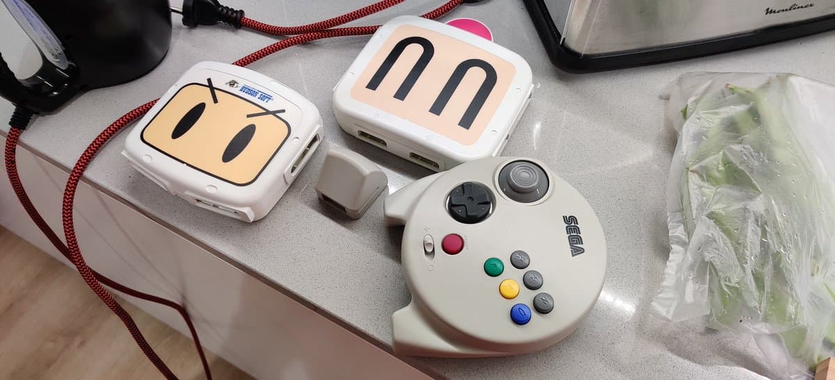 Retrobrighting batch: two white gaming controllers with character faces, heating pad with dual coils, and white game controller with colored buttons on work surface.