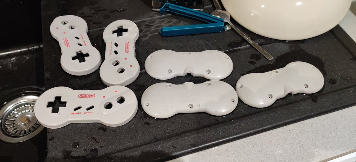 White Nintendo controllers in various stages of retrobrighting on black surface, showing yellowing reversal treatment.