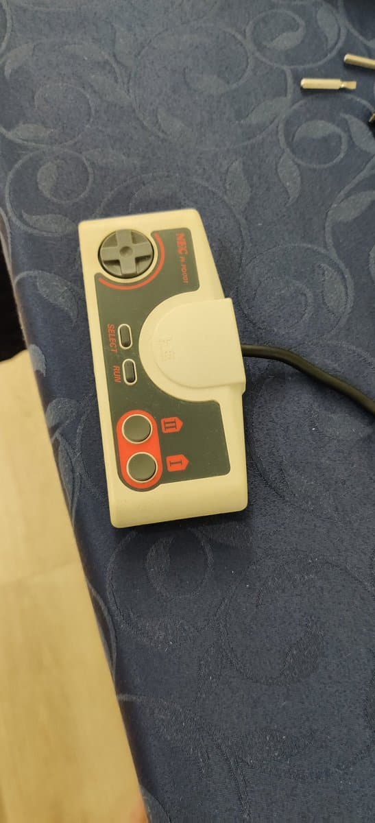 Cream and dark gray retrobrighted game controller on patterned fabric, showing improved plastic coloring from yellowing restoration treatment.