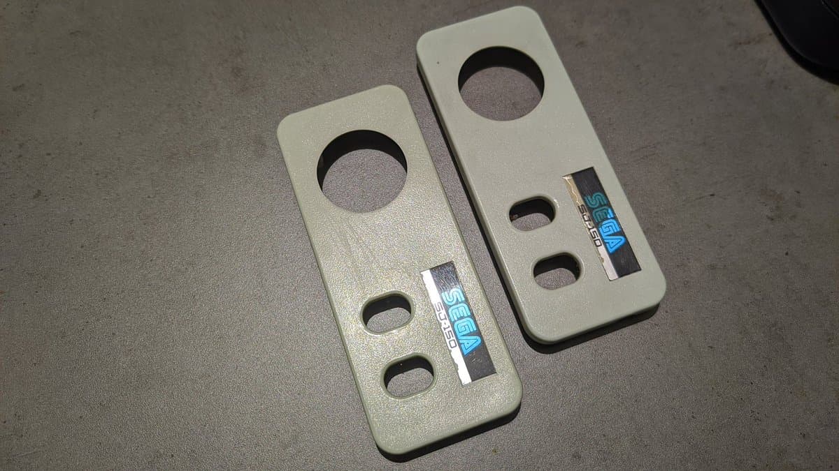 Two cream-colored Sega SG-1000 II controllers after retrobrighting, showing brightened plastic with circular button holes and manufacturer labels visible.