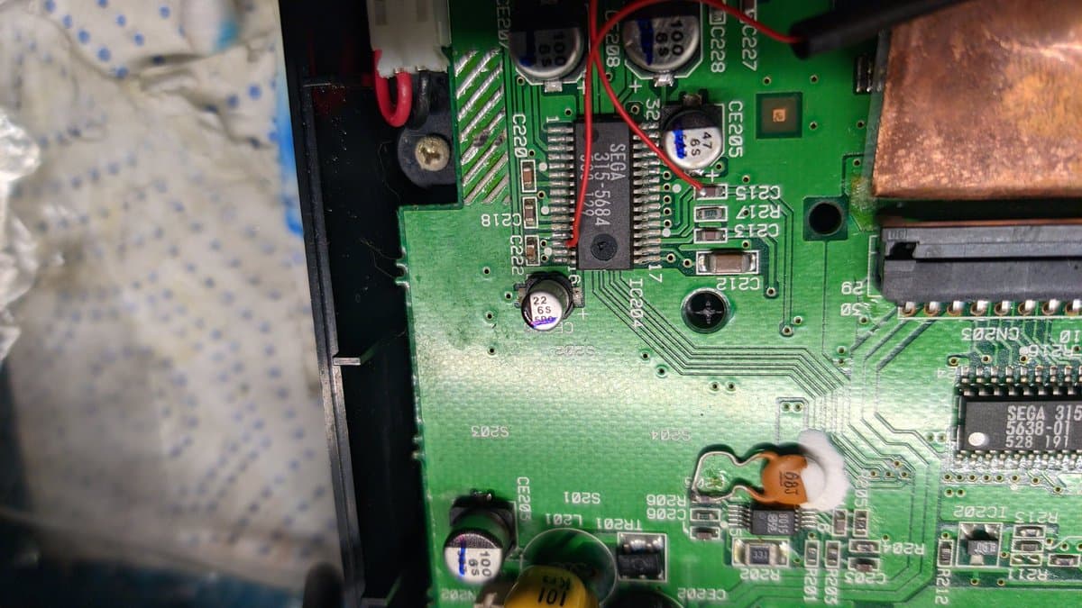 Sega Nomad mainboard with capacitors being removed via soldering iron twist method during restoration; visible corrosion and component damage.