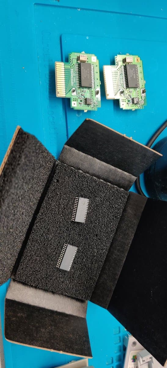 Two N64 Controller Pak PCBs with F-RAM chips installed, displayed above foam storage case containing additional memory modules.