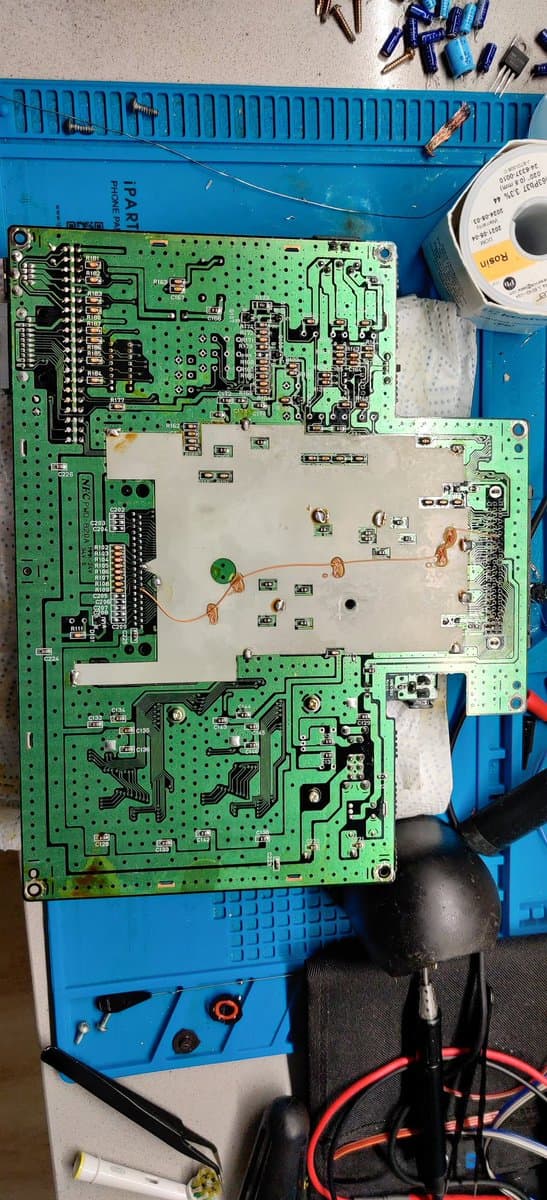 PC Engine SuperGrafx motherboard mid-repair on blue mat, showing new capacitors, voltage regulator replacement, and soldering work in progress with tools nearby.