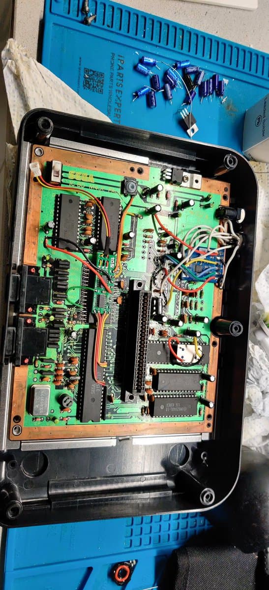 Master System II motherboard with new capacitors installed and voltage regulator replacement in progress; green PCB with IC chips and wiring visible.
