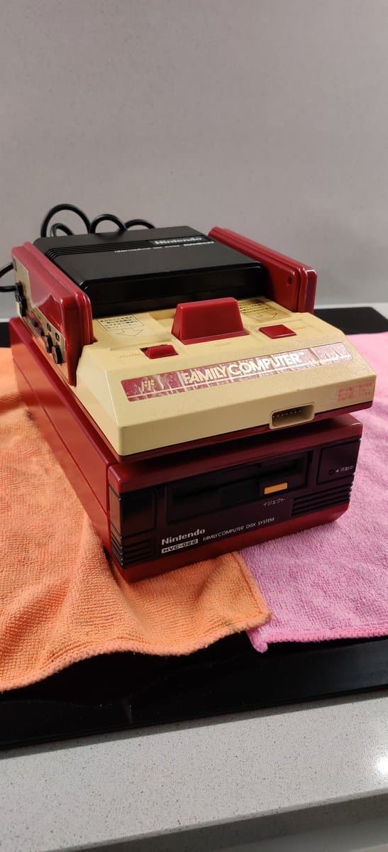 Red and cream Nintendo Famicom with composite mod board installed, displayed with replacement fuse and cleaning cloth during repair documentation.