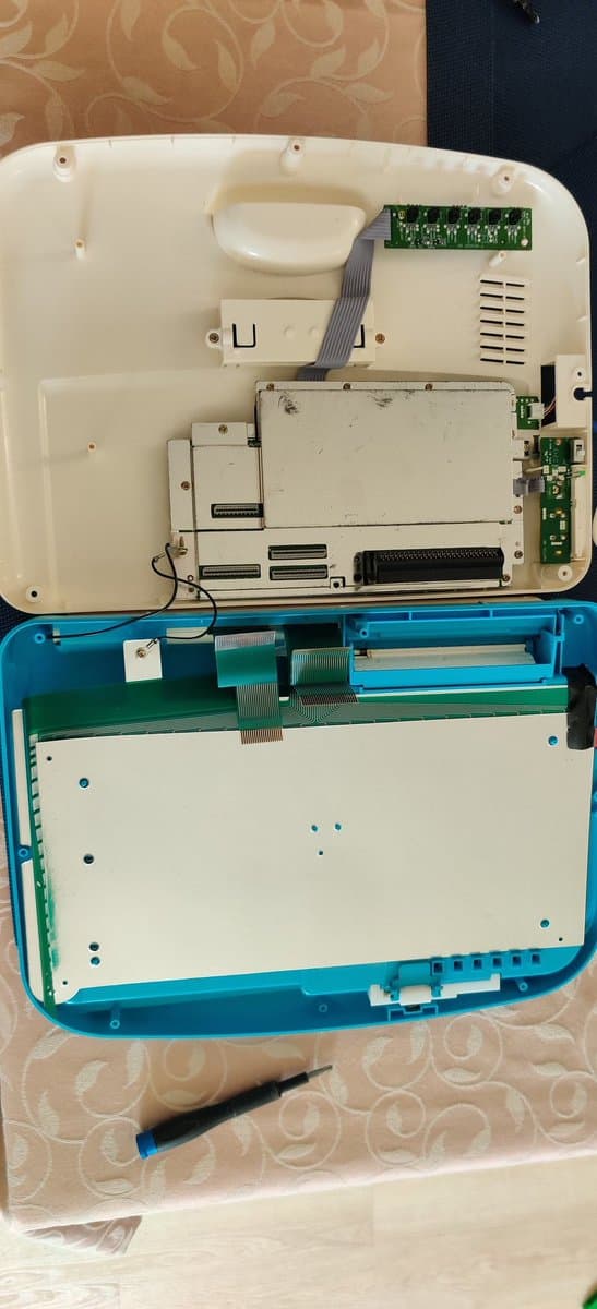 Disassembled Sega Pico showing recap work: motherboard with new capacitors, power regulator, and green circuit boards alongside blue plastic housing and screwdriver.
