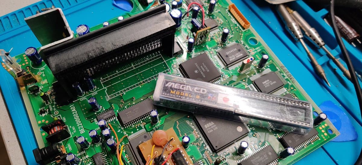 Mega-CD 2 mainboard with region-free BIOS chip installed, showing recapped circuitry, IC chips, and soldering work during restoration.