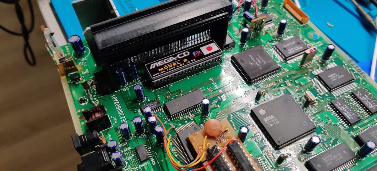 Sega Mega-CD 2 motherboard with desoldering tool removing components during region-free BIOS installation and recapping restoration work.