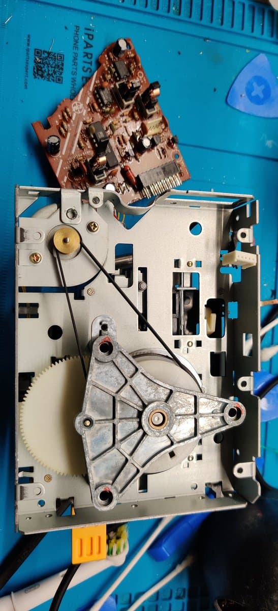 Famicom Disk System disassembled showing motor assembly, white chassis with gears and mechanical components, red circuit board removed above.